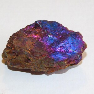 Puede incluir: Una roca rugosa e iridiscente con un color azul, morado y cobre. La roca tiene una forma natural e irregular.
