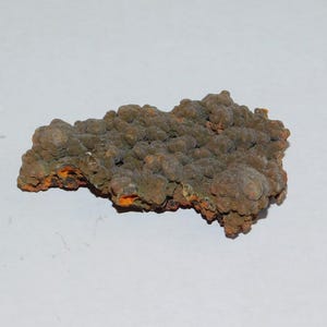 May include: A close-up of a rock formation with a textured surface. The rock has a mix of colors, including brown, orange, and green. The surface is covered in small, rounded bumps.