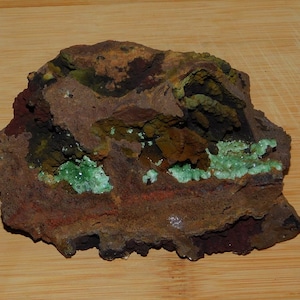 May include: A rough, dark brown rock with green crystals embedded in it. The rock has a layered appearance with different shades of brown and black.