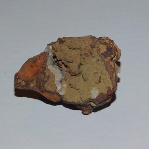 May include: A rough, brown and orange rock with white mineral deposits. The rock has a textured surface and is irregularly shaped.