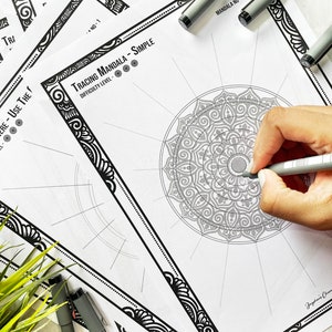 May include: A black and white mandala tracing sheet with the text "Tracing Mandala - Simple" and "Difficulty Level" with a black and white ornate border. The sheet is on a white surface with a hand holding a gray pen tracing the mandala.