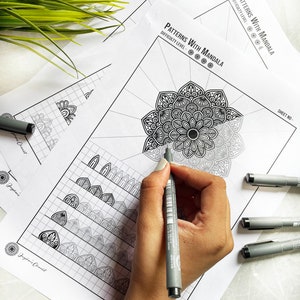 May include: A person's hand is using a black pen to colour a mandala design on a printed page. The page is labelled "Patterns With Mandala" and shows a difficulty level. Other pages and pens are also visible.