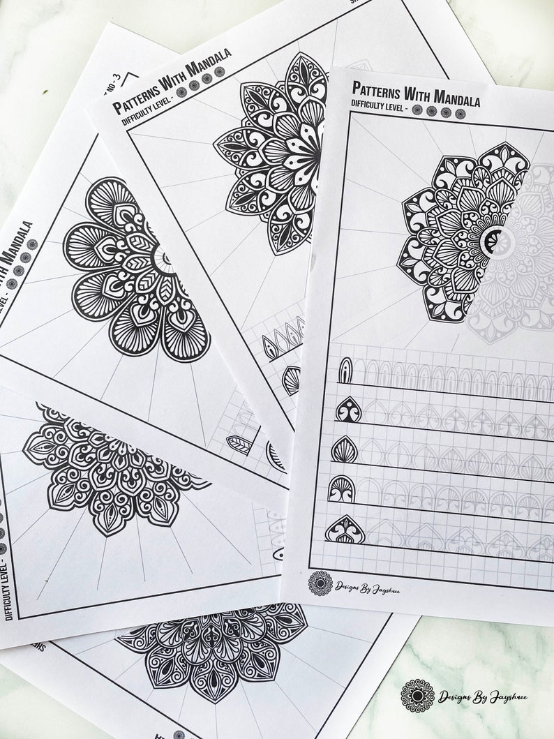 May include: A stack of white paper sheets featuring intricate black and white mandala designs. The text "Patterns With Mandala" and "Difficulty Level" are printed at the top. The bottom right corner of the sheets has the text "Designs By Jayshue".