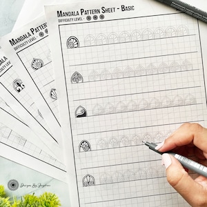May include: A stack of white mandala pattern sheets with a grid background. The sheets are labeled "Mandala Pattern Sheet - Basic" and feature various mandala designs. A black pen is held over one sheet, ready to draw. The difficulty level is indicated by circles.