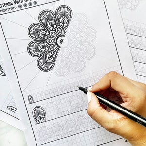 May include: Black and white mandala pattern sheets with the text "PATTERNS WITH MANDALA" and "SHEET NO-3". A hand is holding a black pen, drawing on the sheet. The sheets have a grid pattern and mandala designs.