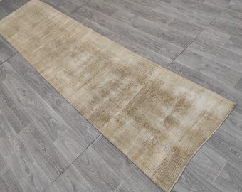 May include: A long, rectangular, off-white rug with a subtle, woven pattern. The rug has a light brown, faded appearance.