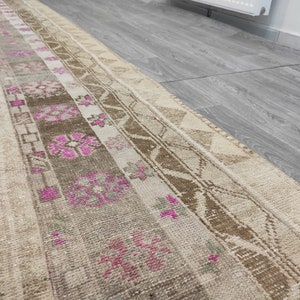 May include: A vintage runner rug with a beige background and a pink and brown geometric pattern. The rug has a distressed look and is made of natural fibers.