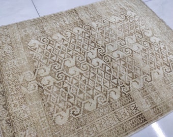 May include: A vintage rug with a beige background and a brown geometric pattern. The rug has a faded look and a worn texture.