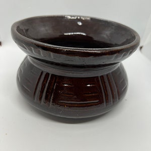 May include: A dark brown ceramic pot with a wide rim and a decorative pattern around the middle. The pot is glazed and has a shiny finish.