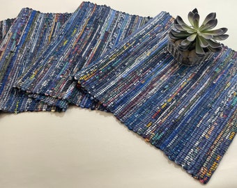 May include: Set of four blue and multi-colored woven placemats. The placemats are made of recycled materials and have a rustic, handmade look.