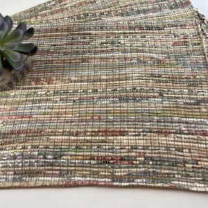 May include: A set of woven placemats in a neutral color palette with brown, beige, and white tones. The placemats are made of a textured material that resembles recycled paper.