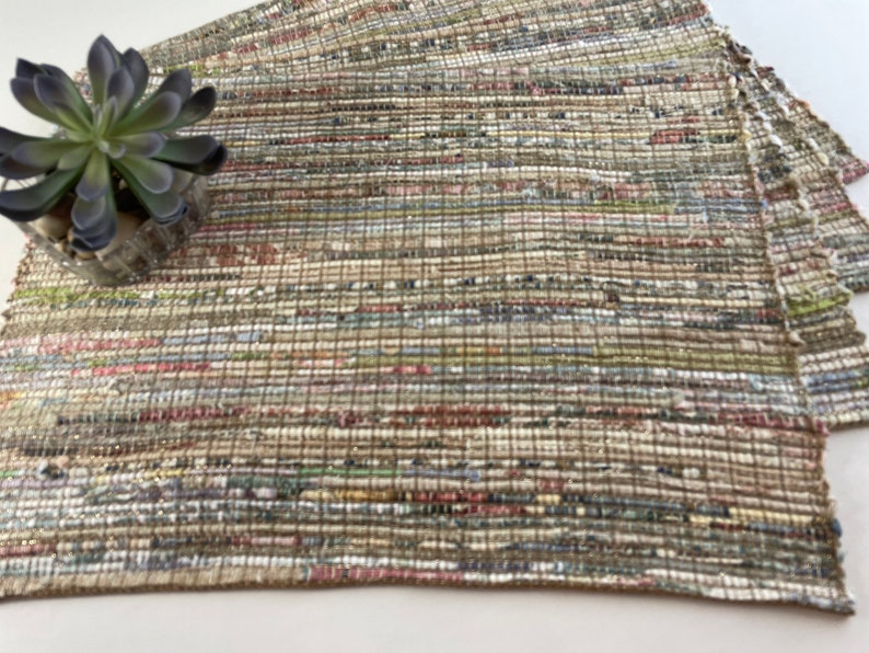 May include: A set of woven placemats in a neutral color palette with brown, beige, and white tones. The placemats are made of a textured material that resembles recycled paper.