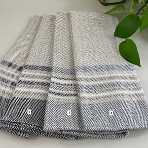 May include: Four kitchen towels with a herringbone pattern and stripes in shades of grey, black, and beige.
