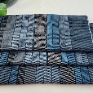 May include: Four blue and gray striped kitchen towels folded on a white surface.