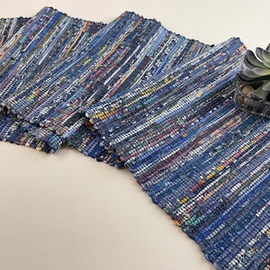 May include: A blue and white woven rug with a colourful, striped pattern. The rug is made from recycled materials and has a fringed edge.