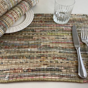 May include: A woven placemat with a multi-colored striped pattern in shades of brown, green, and pink. A white plate, a glass, a knife, a fork, and a spoon are placed on the placemat.
