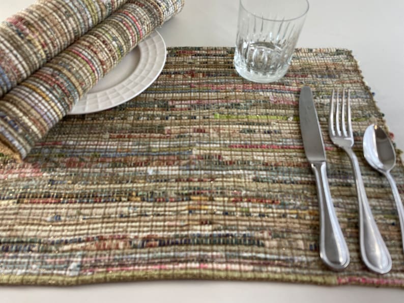 May include: A woven placemat with a multi-colored striped pattern in shades of brown, green, and pink. A white plate, a glass, a knife, a fork, and a spoon are placed on the placemat.