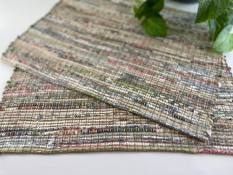May include: Two woven placemats in a neutral color palette with a variety of textures. The placemats are made of recycled materials and have a rustic, handmade look.