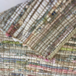 May include: Close-up of a woven rug with a multi-colored pattern. The rug is made of a variety of materials, including cotton, wool, and jute. The rug has a textured surface and a slightly distressed look.