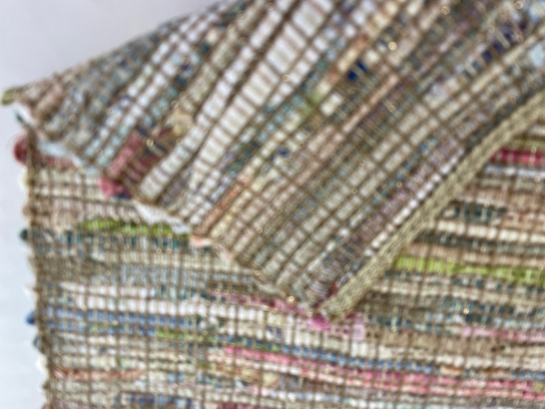 May include: Close-up of a woven rug with a multi-colored pattern. The rug is made of a variety of materials, including cotton, wool, and jute. The rug has a textured surface and a slightly distressed look.