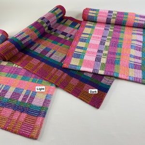 May include: Three woven table runners in pink, purple, green, blue, and orange with a plaid pattern. The runners are labelled "Light" and "Dark".
