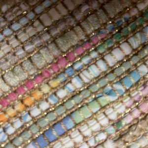 May include: Close-up of a woven rug with a textured, multi-colored pattern. The rug is made of a variety of fabrics, including cotton, linen, and wool. The rug has a subtle sheen, giving it a luxurious look.