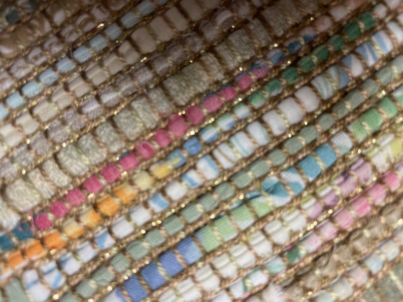 May include: Close-up of a woven rug with a textured, multi-colored pattern. The rug is made of a variety of fabrics, including cotton, linen, and wool. The rug has a subtle sheen, giving it a luxurious look.