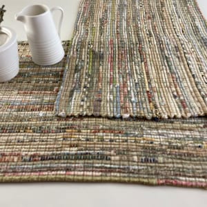 May include: Two woven placemats in a beige, brown, and white color scheme. The placemats are made of recycled materials and have a rustic, handmade look.