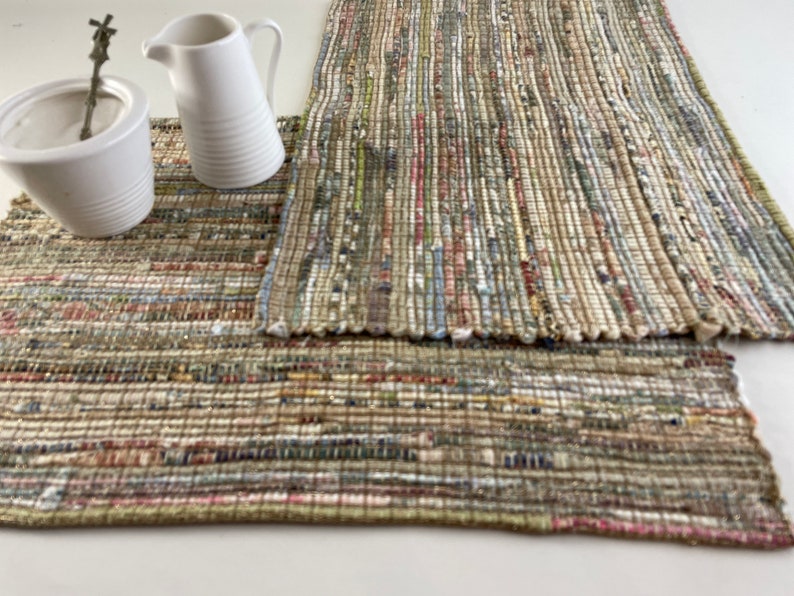 May include: Two woven placemats in a beige, brown, and white color scheme. The placemats are made of recycled materials and have a rustic, handmade look.
