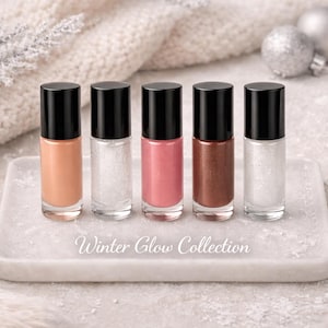 May include: Five nail polish bottles with black caps and various shades of color, including nude, white glitter, pink, bronze, and white glitter, are displayed on a white marble tray. The text "Winter Glow Collection" is written on the tray.