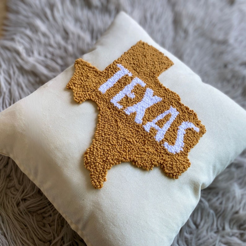 K&ouml;nnte beinhalten: Ein wei&szlig;es Kissen mit einer senfgelben Umrandung des Bundesstaates Texas und dem Wort "TEXAS" in wei&szlig;en Buchstaben.