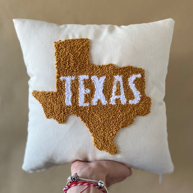 K&ouml;nnte beinhalten: Ein wei&szlig;es Kissen mit einer gelben Umrandung des Bundesstaates Texas und dem Wort "TEXAS" in wei&szlig;en Buchstaben.
