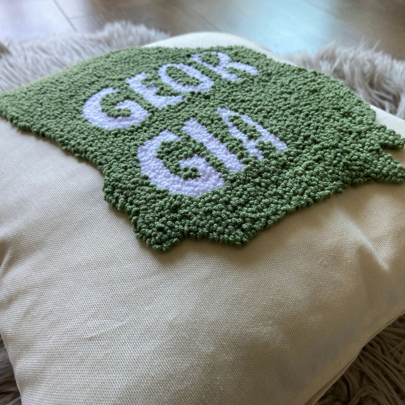 K&ouml;nnte beinhalten: Ein gr&uuml;nes und wei&szlig;es Kissen mit der Aufschrift "GLOW GIRL" in wei&szlig;en Buchstaben.