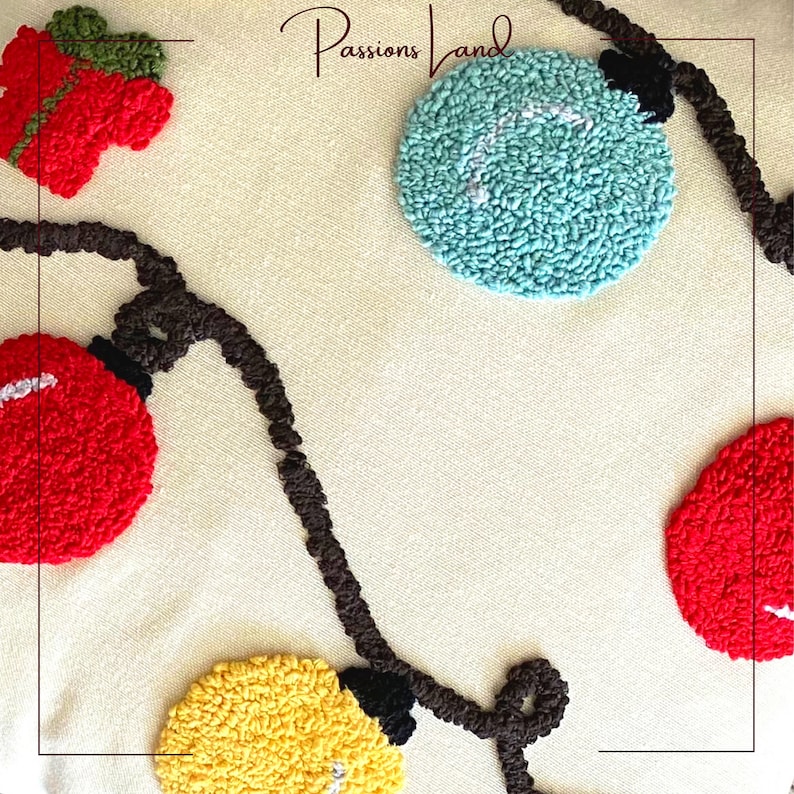 Puede incluir: Una almohada blanca con una cadena de luces marrones, adornos circulares rojos, amarillos y azules, y el texto "Passions Land".
