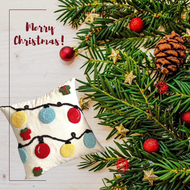 Puede incluir: Una almohada blanca con un dise&ntilde;o de luces de Navidad bordado. La almohada presenta adornos rojos, amarillos, azules y verdes, as&iacute; como peque&ntilde;as cajas de regalo. La almohada est&aacute; rodeada de ramas de pino con bayas rojas y estrellas doradas.