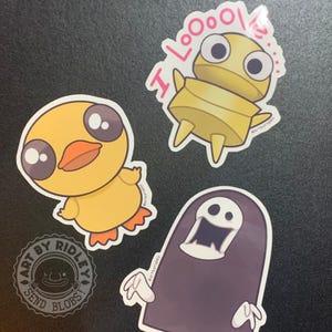 May include: A collection of cartoon stickers featuring a yellow duckling, a mummy with the text "I LoooOoo!", and a purple ghost. The stickers are designed with bold outlines and bright colors.