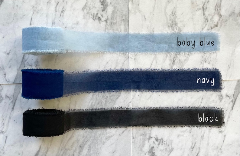 Pu&ograve; includere: Tre rocchetti di nastro con bordi sfilacciati disposti orizzontalmente. Il nastro superiore &egrave; azzurro, quello centrale &egrave; blu navy e quello inferiore &egrave; nero. Ogni rocchetto &egrave; etichettato con il nome del colore in semplice testo nero.