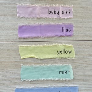 Pu&ograve; includere: Sei strisce rettangolari di tessuto con bordi sfilacciati disposte verticalmente. I colori sono etichettati come rose ash, baby pink, lilac, yellow, mint e powder blue. Ogni striscia presenta una consistenza opaca morbida e un bordo grezzo.