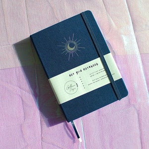 Dot Grid Journal, Dot Grid Journal, Travel Journal, Reading Journal, Journals and Notebooks, Junk Journal, Dot Grid Notebook, Halloween Gift. A dark blue dot grid notebook with a silver crescent moon and sun design. The notebook has a white label that says 'dot grid notebook'.