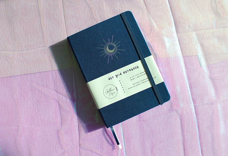 Dot Grid Journal, Dot Grid Journal, Travel Journal, Reading Journal, Journals and Notebooks, Junk Journal, Dot Grid Notebook, Halloween Gift. A dark blue dot grid notebook with a silver crescent moon and sun design. The notebook has a white label that says 'dot grid notebook'.