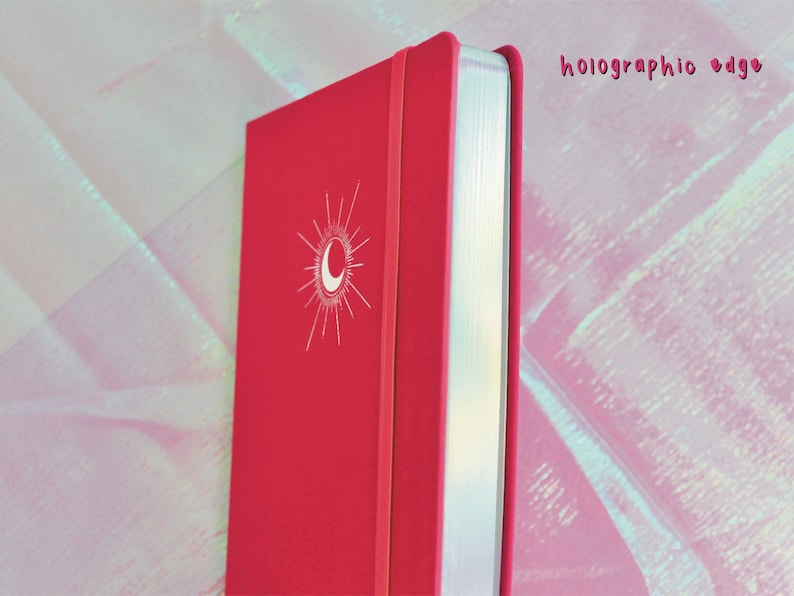 A pink hardcover journal with a white moon and sun design on the front cover. The edge of the journal is silver and has a holographic finish. Dot Grid Journal, Dot Grid Journal, Travel Journal, Reading Journal, Journals and Notebooks, Junk Journal, Dot Grid Notebook, Halloween Gift