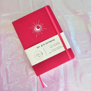 A pink dot grid notebook with a white moon and sun design on the cover. The notebook has a white label that says 'dot grid notebook'. Dot Grid Journal, Dot Grid Journal, Travel Journal, Reading Journal, Journals and Notebooks, Junk Journal, Dot Grid Notebook, Halloween Gift