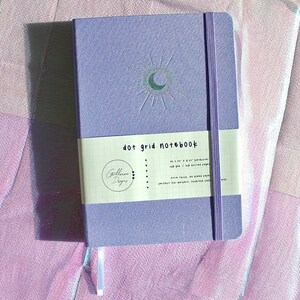 A purple dot grid notebook with a silver moon and sun design. The notebook has a white label that reads 'dot grid notebook'. Dot Grid Journal, Dot Grid Journal, Travel Journal, Reading Journal, Journals and Notebooks, Junk Journal, Dot Grid Notebook, Halloween Gift