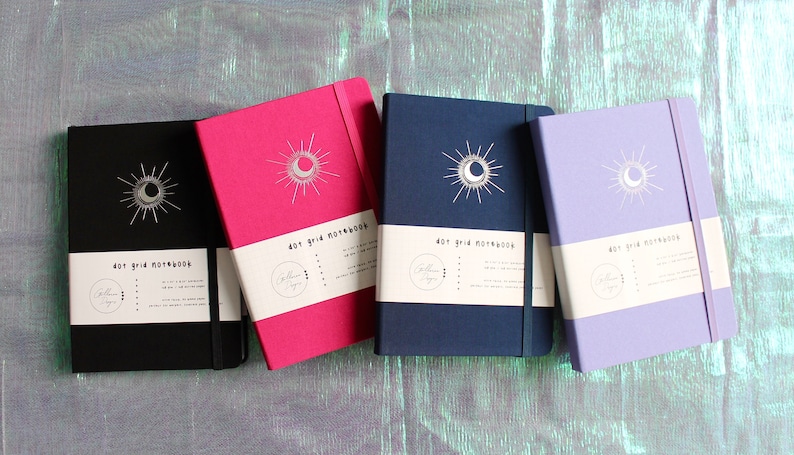 Four dot grid notebooks with a moon and sun design. The notebooks are black, pink, blue, and purple. Each notebook has a white label that reads 'dot grid notebook'. Dot Grid Journal, Dot Grid Journal, Travel Journal, Reading Journal, Journals and Notebooks, Junk Journal, Dot Grid Notebook, Halloween Gift