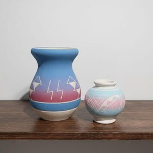 May include: A white ceramic mug with a black handle and the text "But First, Coffee" in a black, handwritten-style font. The mug is on a white surface.