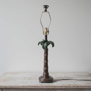 May include: A bronze-colored table lamp with a palm tree design. The lamp features a detailed palm tree trunk base, green palm fronds, and a small palm tree at the top. The lamp is approximately 28 inches tall.