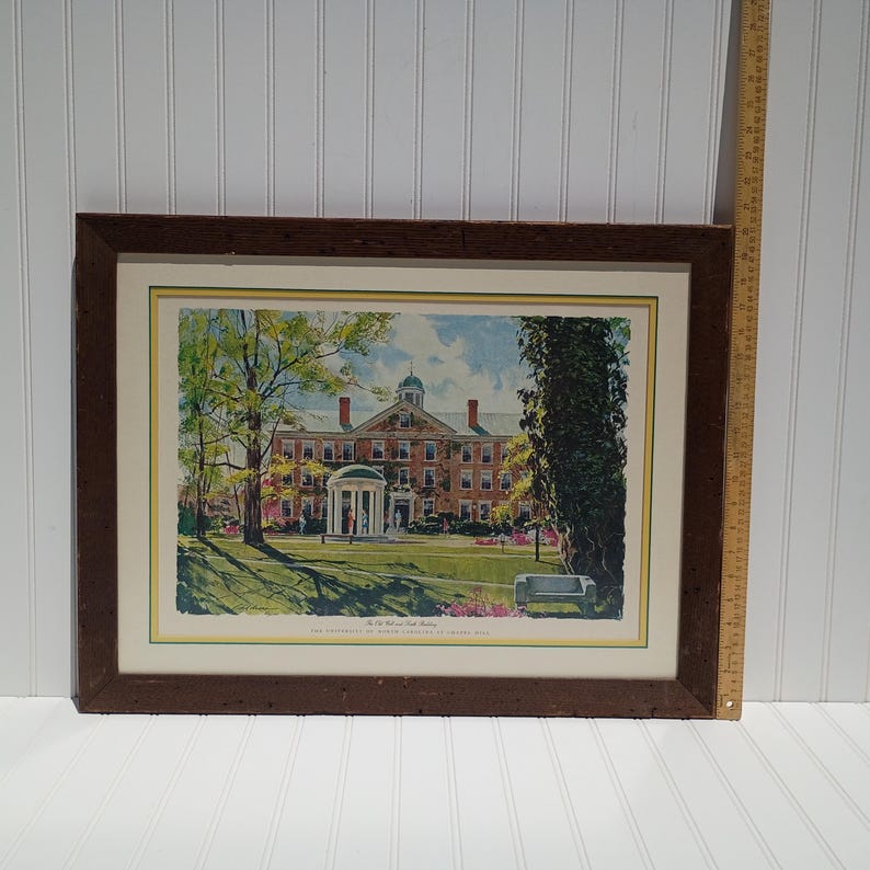 Op de afbeelding: Ingelijste prent van een universiteitsgebouw met een groot gazon en bomen. Het gebouw is van baksteen met een koepeldak en zuilen. De lijst is van donkerbruin hout.