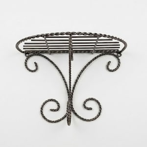 May include: A dark brown metal wall shelf featuring a semi-circular top platform with horizontal slats. The structure is supported by two decorative, curved scrollwork brackets made of twisted metal rods, providing a sturdy and open design.