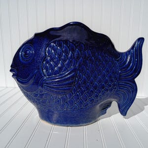 May include: A ceramic fish-shaped decorative bowl in a deep blue hue. The bowl features textured scales, fins, and a detailed face. The top edge is wavy, and the bowl has a crackled glaze finish, adding to its vintage appeal.