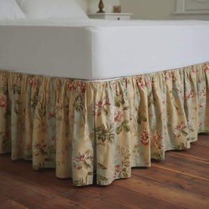 May include: A bed skirt with a floral pattern in shades of cream, light blue, and red. The fabric is gathered, creating a ruffled effect. The bed skirt is designed to hang from the bed frame, concealing the box spring.